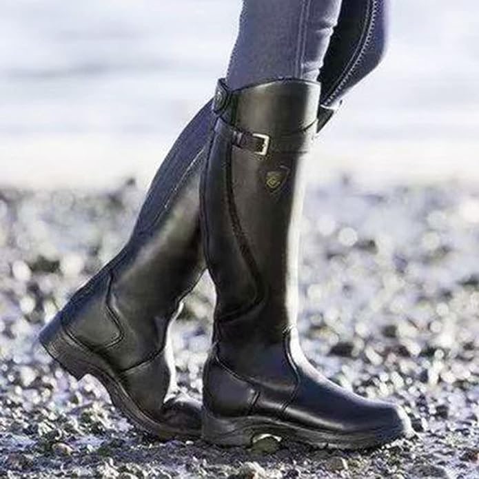 A close-up shot shows a person wearing black tall riding boots and dark pants, standing on a pebbled ground.