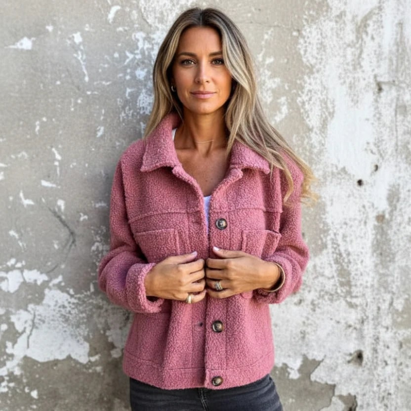 Front view of a woman wearing a pink sherpa fleece shacket with a white top and dark jeans, holding the front opening.