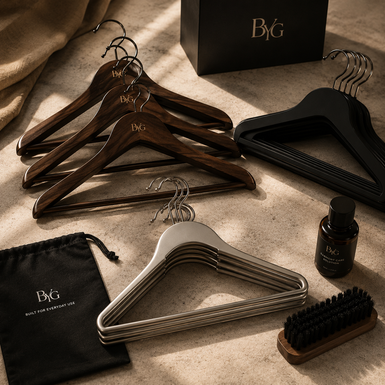 Flat lay of premium wooden, velvet and stainless steel clothes hangers with wardrobe care accessories on a neutral surface.