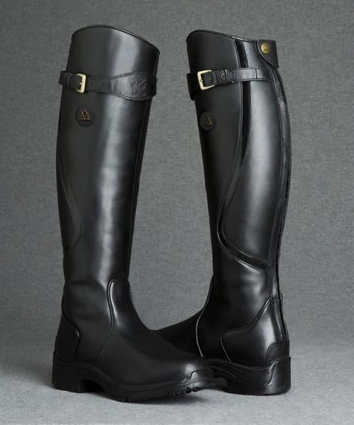 A pair of black tall riding boots with buckle details and zippers, standing upright in a studio setting.