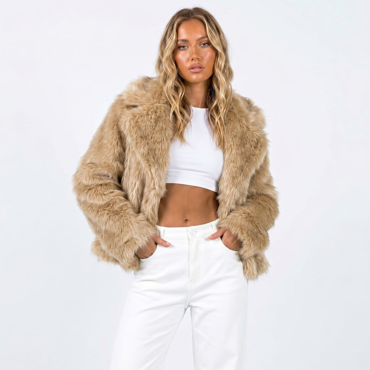 Front view of a woman wearing a tan cropped faux fur jacket over a white crop top and white pants.