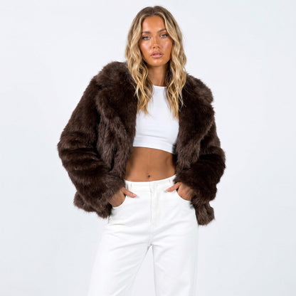 Front view of a woman wearing a dark brown cropped faux fur jacket over a white crop top and white pants.