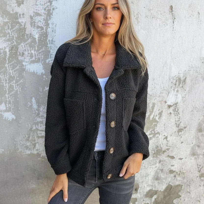 Front view of a woman wearing a dark grey sherpa fleece shacket with a white top and dark jeans.