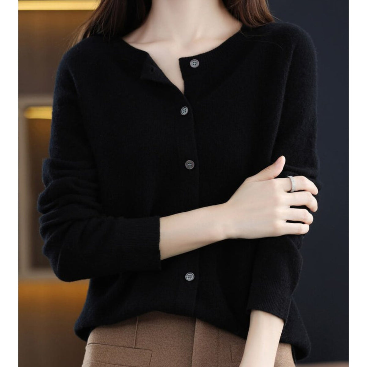 Front view of a woman wearing a black fine knit button-front cardigan, styled with the top button undone.