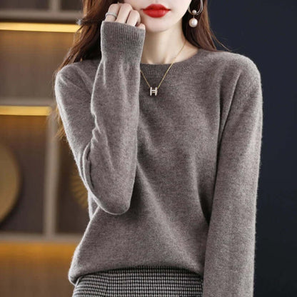 Front view of a woman wearing a grey fine-knit crew neck sweater, showing ribbed cuffs.