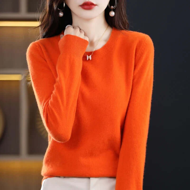 A model wears an orange long-sleeved crew neck sweater, accessorized with a gold 'H' pendant necklace.