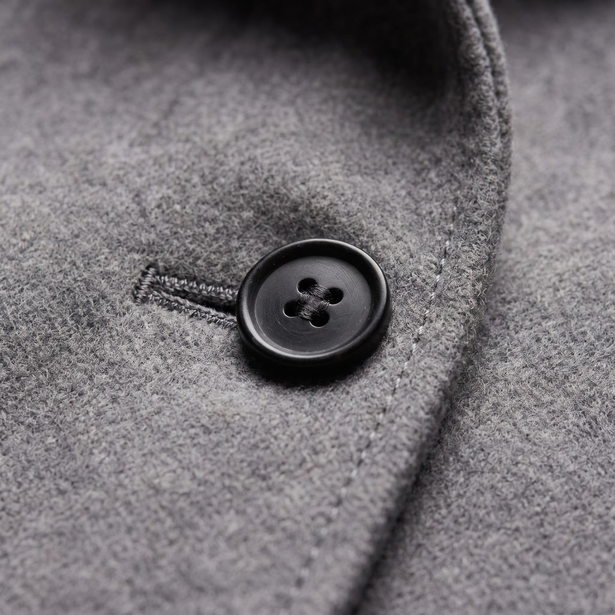 Close-up detail of a black button and buttonhole on the grey wool blend coat.