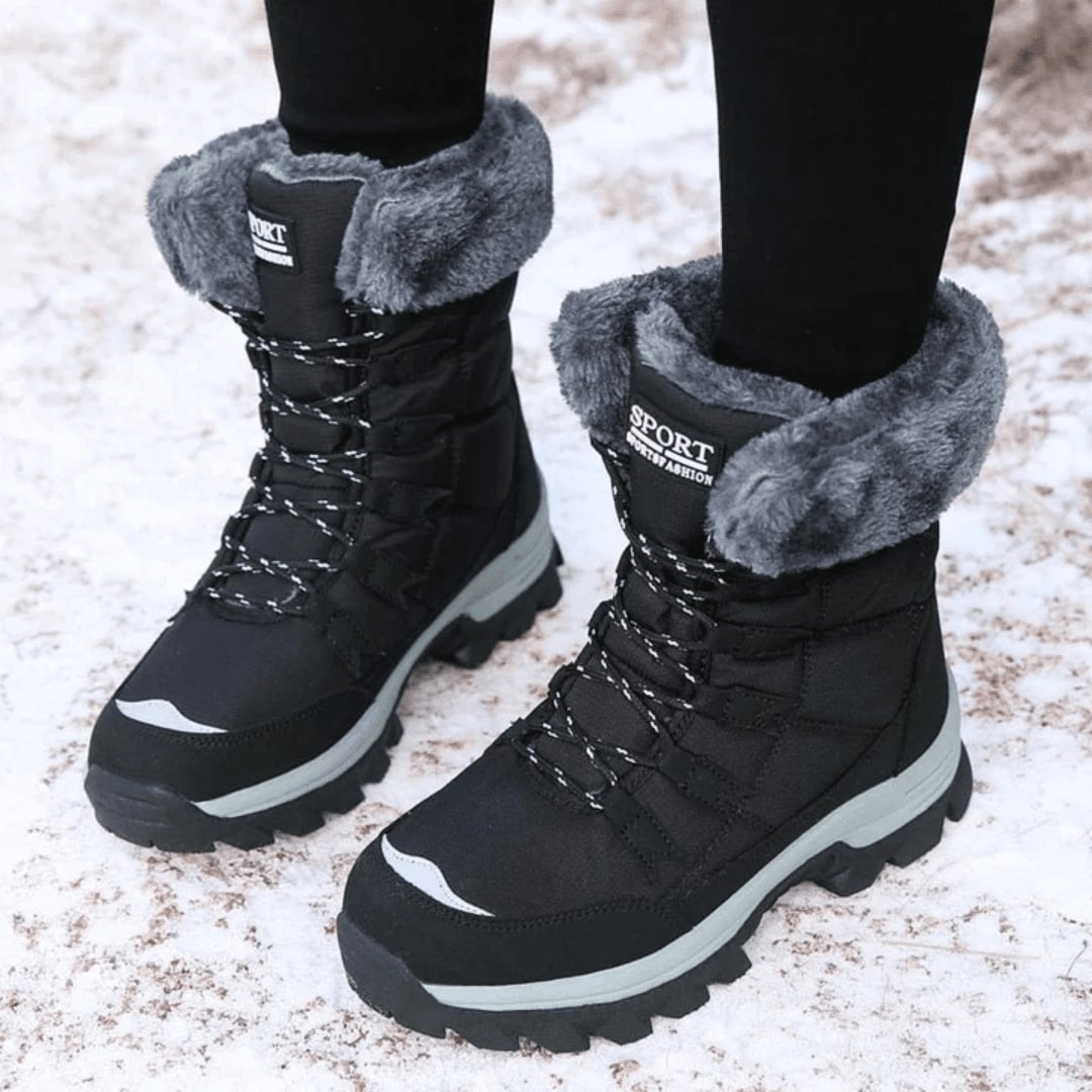 Front view of black faux fur lined snow boots worn on feet in snow.