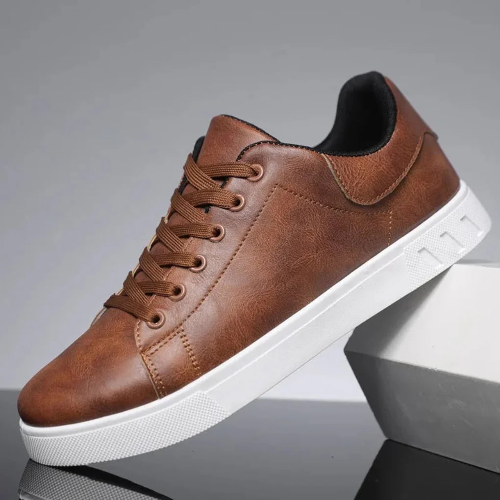A single brown faux leather low-top sneaker with white sole is displayed at an angle on a reflective surface.