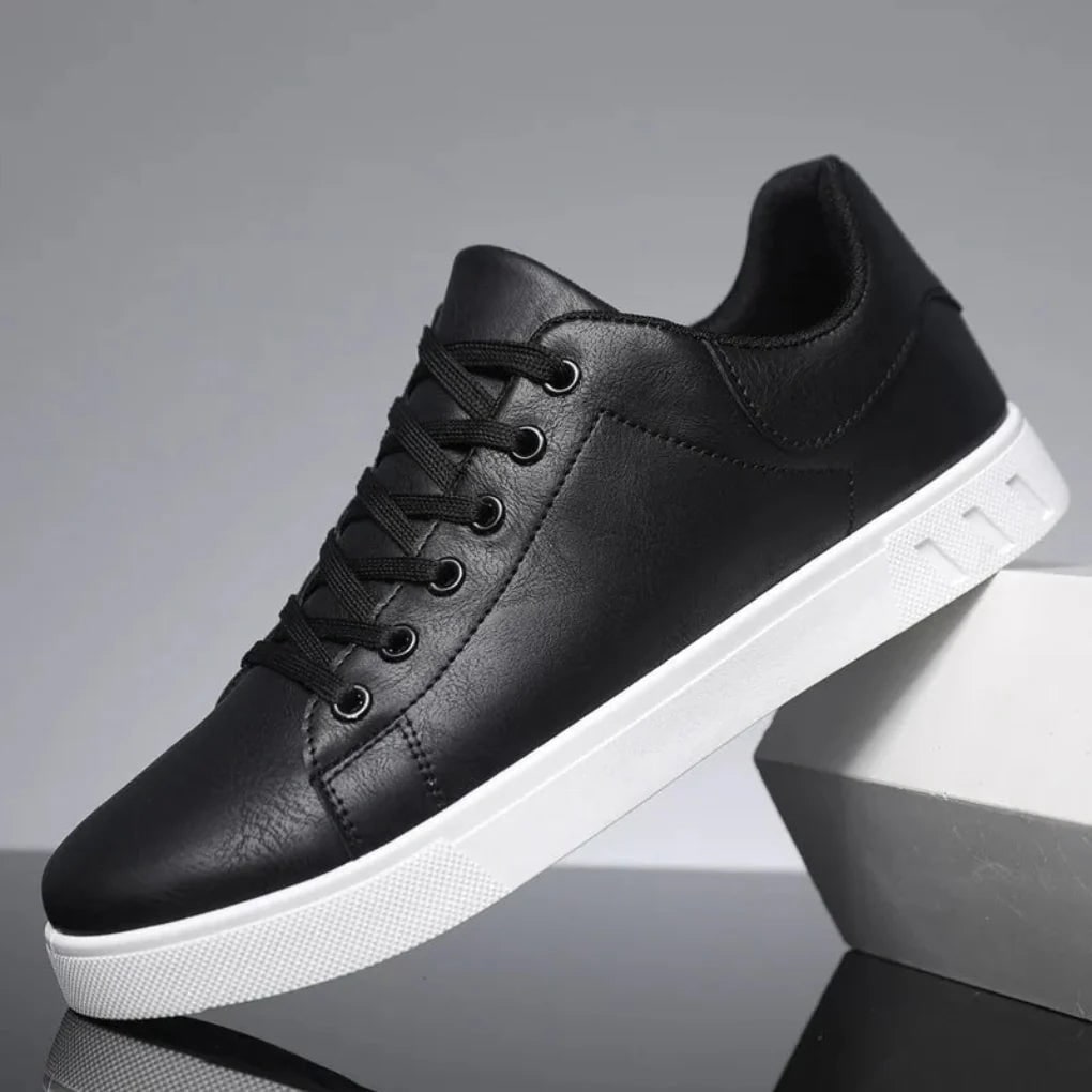 A single black faux leather low-top sneaker with white sole is displayed at an angle on a reflective surface.