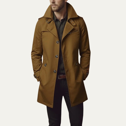 Front view of a man wearing a brown single-breasted trench coat with a patterned shirt and dark trousers.