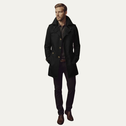 Full body front view of a man wearing a black single-breasted trench coat, patterned shirt, dark trousers, and brown shoes.