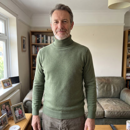 Front view of a man wearing a sage green turtleneck sweater in a living room setting.