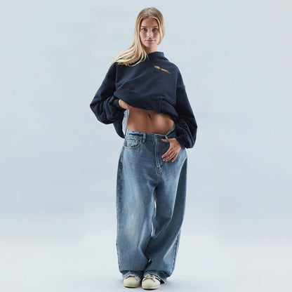 On-model front view of a dark blue oversized hoodie, with the model lifting the hem to reveal her midriff.