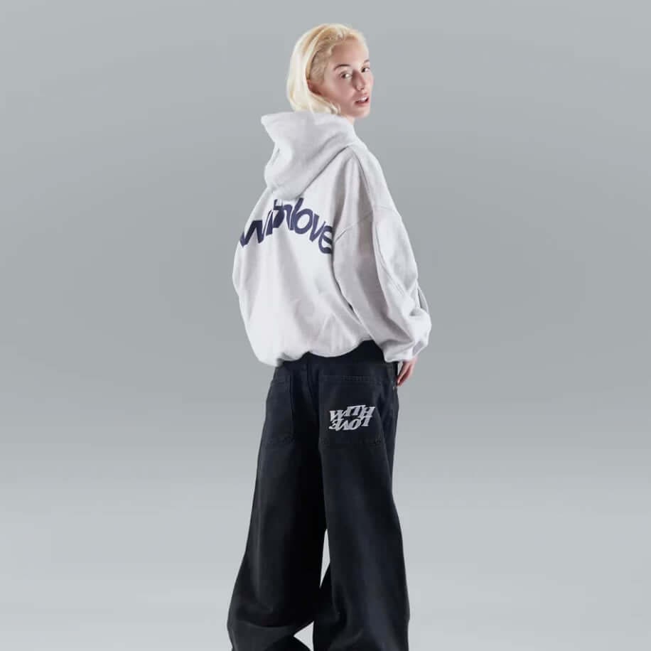 On-model back view of a light grey oversized hoodie with a large 'withlove' graphic, worn with black baggy jeans.